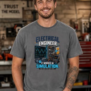 Può includere: Una t-shirt a maniche corte grigio antracite con una stampa grafica di un impianto di ingegneria elettrica con monitor del computer, pannello di circuito e multimetro. Il testo recita: ELECTRICAL ENGINEER IT WORKED IN SIMULATION. THAT WAS THE EASY PART.