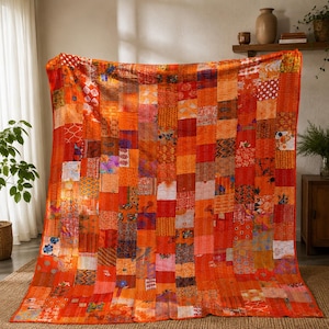 Könnte beinhalten: Eine große rechteckige Decke mit einem Patchwork-Design, das aus zahlreichen kleinen Stoffquadraten in verschiedenen Orange-, Rot- und Gelbtönen besteht. Die Decke zeigt eine Vielzahl von komplizierten Mustern, Blumenmotiven und geometrischen Drucken.