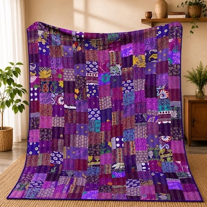Op de afbeelding: Een rechthoekige quilt met een patchworkontwerp bestaande uit talloze stoffen vierkanten in diverse tinten paars, violet en magenta. De quilt toont een verscheidenheid aan ingewikkelde patronen, waaronder bloemmotieven, paisley en geometrische vormen.