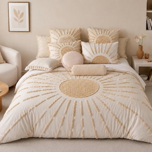 May include: A cream-coloured bedding set featuring a tufted sunburst design in a tan hue. The set includes a duvet cover, two square pillows with sunburst patterns, a rectangular pillow, a round pillow, and a cylindrical bolster pillow.