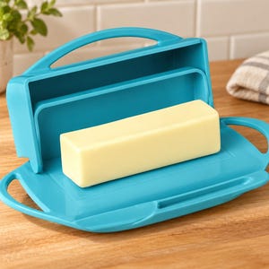 Op de afbeelding: Een fel turquoise plastic botervloot met een scharnierend deksel en geïntegreerde handgrepen aan de zijkanten. De botervloot staat open en toont een rechthoekig blok lichtgele boter op de platte bodem met afgeronde randen.