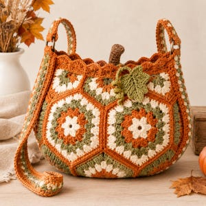 May include: A crochet handbag featuring a pumpkin-inspired design made from hexagonal granny squares in shades of orange, cream, and olive green. The bag includes a brown stem, a textured green leaf accent, and two sturdy crocheted shoulder straps.