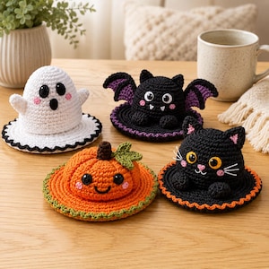 Puede incluir: Cuatro figuras de ganchillo que incluyen un fantasma blanco, un murciélago negro con alas moradas, una calabaza naranja con una hoja verde y un gato negro. Cada figura está unida a una base circular con un borde festoneado y mejillas rosas.
