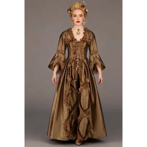 May include: A floor-length bronze-colored gown featuring long flared sleeves, a lace-up bodice, and vertical ruffled trim down the front. The dress has a V-neckline and is paired with a pearl choker necklace and matching drop earrings.
