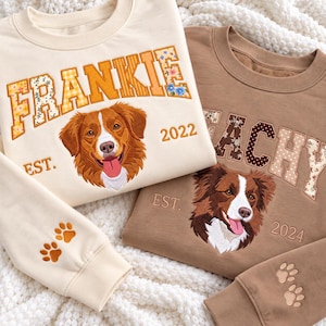 May include: A cream sweatshirt with the embroidered name FRANKIE, a brown dog portrait, and EST. 2022, plus a brown sweatshirt with the name PEACHY, a brown and white dog portrait, and EST. 2024. Both sleeves feature embroidered paw prints.