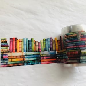 May include: A roll of colorful washi tape with a pattern of stacked books. The tape is printed with a watercolor effect and features a variety of colors, including blue, green, red, yellow, and orange.