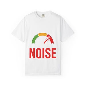 May include: A white short-sleeve t-shirt featuring a graphic of a semi-circular gauge with green, yellow, and red segments. A red needle points into the red zone, which includes a small triangle icon. The word NOISE is printed in large red letters.