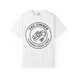 以下が含まれることがあります： 胸元に黒い円形のグラフィックがプリントされた白い半袖Tシャツ。デザインにはOBD2診断スキャナーのイラストと、その中央のアイコンを囲むように円状に配置されたVAG OWNER CLEARING CODES, CHEAPというテキストが含まれています。