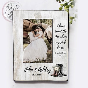 May include: A white wooden picture frame with a black border. The frame has a photo of a couple in a field with a horse. The text "I have found the One whom my soul loves. Song of Solomon 3:4" is printed on the frame. The names "John & Ashley" and the date "06.24.2023" are also printed on the frame.