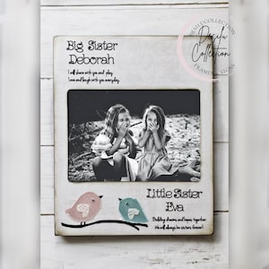 May include: White wooden picture frame with a black and white photo of two girls. The frame has the text "Big Sister Deborah" and "Little Sister Eva" with a bird design on the bottom.