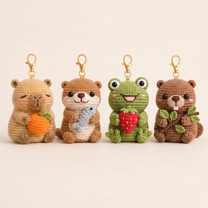 May include: Four crochet animal keychains featuring a tan capybara holding an orange, a brown otter holding a blue fish, a green frog holding a red strawberry, and a brown beaver holding a green branch, each with a gold-toned metal lobster clasp.