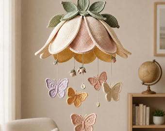 May include: A hanging mobile featuring a large, crocheted flower in shades of cream, pale pink, and yellow with sage green leaves at the top. Suspended from the flower are several crocheted butterflies in lavender, yellow, peach, and cream.