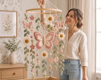 May include: A hanging mobile featuring a circular wooden frame with crocheted elements including a large central butterfly, smaller butterflies, various flowers, and green leaf vines in shades of pink, cream, and sage green, suspended by white strings.