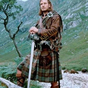 Puede incluir: Un conjunto tradicional de kilt que incluye una chaqueta de cuero marrón, una falda de lana a cuadros en tonos verdes y marrones, un esporrán de cuero y botas marrones con cordones. El conjunto incluye una manta de hombro con un broche metálico.