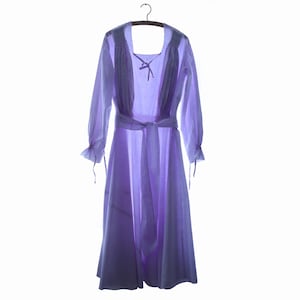 May include: A light purple long-sleeved dress featuring a square neckline with a tie closure, gathered fabric at the shoulders, and a matching fabric belt tied at the waist. The sleeves have ruffled cuffs with thin ties, and the skirt is full-length.
