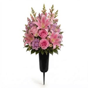 May include: A floral arrangement featuring pink lilies, pink roses, lavender carnations, and tall snapdragons in shades of pink and purple. The flowers are contained within a black, tapered, spike-based vase designed for insertion into the ground.