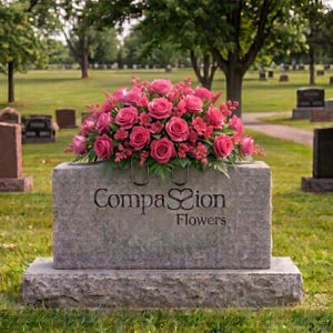 May include: A rectangular grey stone monument features a floral arrangement of vibrant pink roses and small filler flowers on top. The front of the stone is engraved with the text Compassion Flowers, with a heart-shaped icon replacing the letter s.