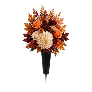 May include: A floral arrangement featuring orange and cream roses, a large cream hydrangea, and dark red flowers, accented with brown and orange autumn leaves. The bouquet is held in a black, tapered, spike-bottomed vase designed for ground insertion.