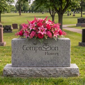 May include: A rectangular grey stone monument features the engraved text Compassion Flowers with a heart symbol between the words. A vibrant floral arrangement of pink lilies, roses, and small filler flowers sits on top.