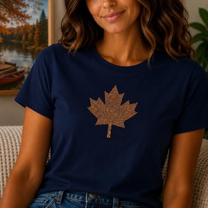 May include: A navy blue short-sleeved t-shirt featuring a large, centered graphic of a maple leaf. The leaf design is rendered in a light orange color and is composed of intricate, swirling lines that resemble a human fingerprint pattern.