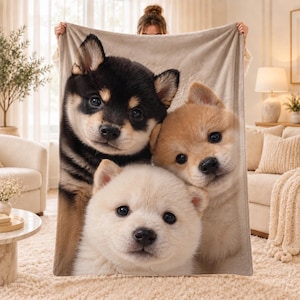 May include: A soft, beige-toned throw blanket featuring a high-definition photographic print of three Shiba Inu puppies. The design displays one black and tan puppy, one light brown puppy, and one cream-colored puppy huddled together closely.