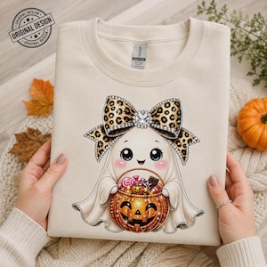 Può includere: Una felpa girocollo color crema con la stampa di un fantasma bianco che indossa un grande fiocco leopardato con strass. Il fantasma tiene in mano un secchiello per dolci a forma di zucca pieno di variopinti caramelle e cioccolatini.