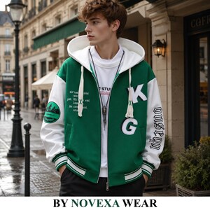 Könnte beinhalten: Eine grün-weiße College-Jacke mit Reißverschluss und Kapuze, verziert mit weißen Buchstaben-Aufnähern K und G auf der Vorderseite, einem kreisförmigen Berggrafik-Motiv am rechten Ärmel sowie weißem Text am linken Ärmel und auf der Brust.