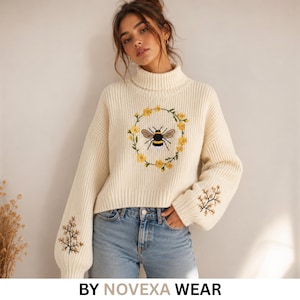 Peut inclure: Un pull en tricot côtelé de couleur crème avec un col roulé et des manches longues. Le centre de la poitrine présente une abeille brodée entourée d'une couronne de fleurs jaunes, avec des broderies de branches fleuries sur chaque manche.