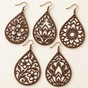 May include: Five teardrop-shaped wooden earrings with intricate laser-cut floral and botanical patterns. Each earring features a dark brown finish and is attached to a brass-toned metal hook for hanging. The designs include various flower motifs.