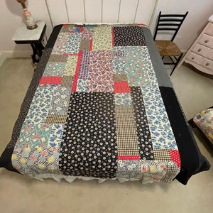 Könnte beinhalten: Eine Patchwork-Decke mit verschiedenen floralen und geometrischen Mustern in Rot-, Blau-, Schwarz- und Weißtönen. Die Decke liegt auf einem Bett mit einem weißen Metallkopfende.