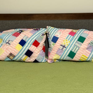 May include: Two rectangular pillowcases featuring a patchwork design composed of various fabric squares in colors including red, blue, yellow, green, and purple, interspersed with light blue and white striped fabric strips throughout the pattern.