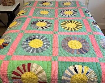 Puede incluir: Una colcha vintage con un diseño de patchwork que presenta un patrón repetitivo de círculos amarillos, rosas y azules. La colcha está hecha de varias telas y se muestra en un marco de cama blanco.