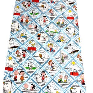 May include: A white and blue Snoopy-themed fabric featuring comic strip panels with Snoopy, Charlie Brown, and other Peanuts characters. The fabric has a diamond grid pattern with phrases like "Happiness is..." and "Forty-nine flavours."