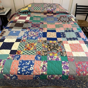 May include: A patchwork quilt with a variety of floral and geometric patterns in shades of pink, blue, green, and brown. The quilt is made of cotton fabric and is quilted with a simple stitch. The quilt is displayed on a bed with a white headboard.