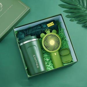Könnte beinhalten: Eine Geschenkbox mit einem dunkelgrünen Kaffeebecher mit der Aufschrift COFFEE, einem dunkelgrünen Regenschirm mit UPF50+-Etikett und einem hellgrünen Handventilator mit kronenförmigem Aufsatz und einem kleinen separaten grünen Sockel.