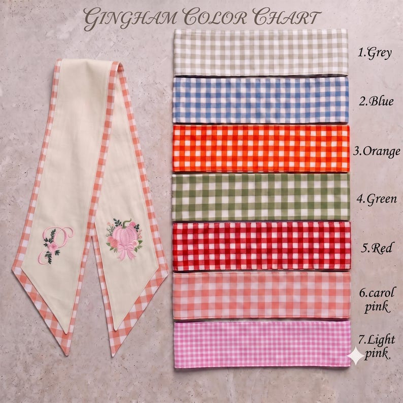 Pu&ograve; includere: Una tabella colori Gingham con una lunga striscia di tessuto color crema con bordi a quadretti arancioni, ricamata con una lettera P e una zucca. A destra ci sono sette campioni di tessuto in grigio, blu, arancione, verde, rosso, rosa carol e rosa chiaro.
