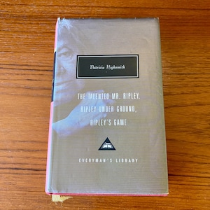 May include: A hardcover book titled "The Talented Mr. Ripley" by Patricia Highsmith. The book has a gray and white striped cover with the author's name and book titles in white text. The book is wrapped in clear plastic.