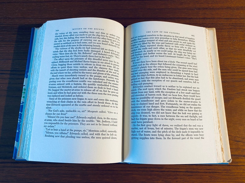 K&ouml;nnte beinhalten: Nahaufnahme von zwei Seiten aus einem Buch mit dem Titel "Mutiny on the Bounty" und "The Last of the Pandora". Die Seiten sind ge&ouml;ffnet, um Text &uuml;ber die Meuterei und die Reise des Schiffes zu enth&uuml;llen. Die Seiten sind gealtert und haben einen abgenutzten, Vintage-Look.