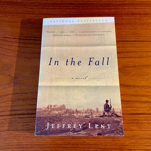 May include: A book cover with the title "In the Fall" by Jeffrey Lent. The cover features a vintage photograph of a soldier standing in a field.