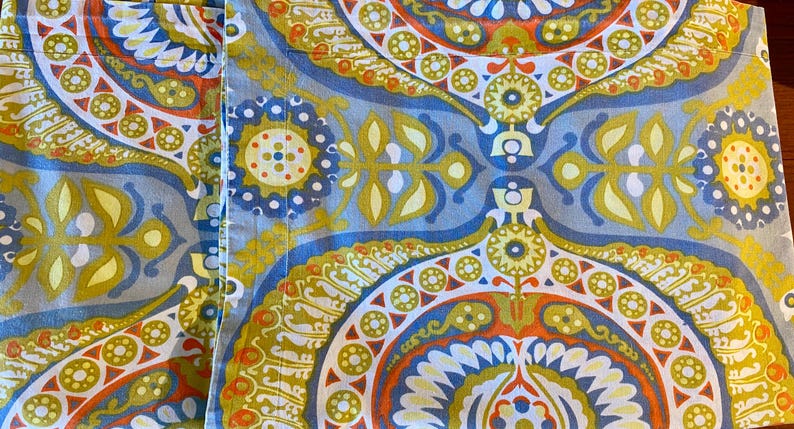 May include: A close-up of a fabric with a blue, green, yellow, orange, and white paisley pattern.