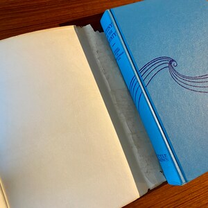 K&ouml;nnte beinhalten: Ein blaues Hardcover-Buch mit dem Titel "Die siebenundzwanzigste Frau" von Colleen McCullough. Der Buchumschlag zeigt ein stilisiertes Wellendesign in Lila.