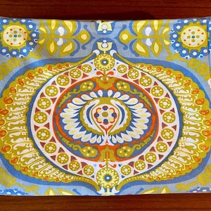 May include: A blue and white fabric with a large, intricate, colorful pattern. The pattern features a central circle with a repeating design of yellow, orange, and red.