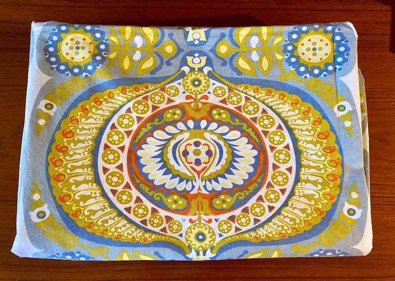 May include: A blue and white fabric with a large, intricate, colorful pattern. The pattern features a central circle with a repeating design of yellow, orange, and red.