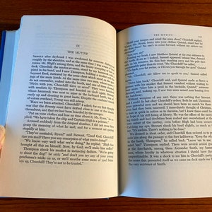 K&ouml;nnte beinhalten: Eine Nahaufnahme eines ge&ouml;ffneten Buches mit gelbem R&uuml;cken. Das Buch tr&auml;gt den Titel "The Mutiny" und der Text auf der Seite handelt von einer Meuterei auf einem Schiff. Der Text lautet "We've mutinied, Byanl!" said Stewart, "Good God, Churchill! Are you mad? Have you any conception of what you're doing?"