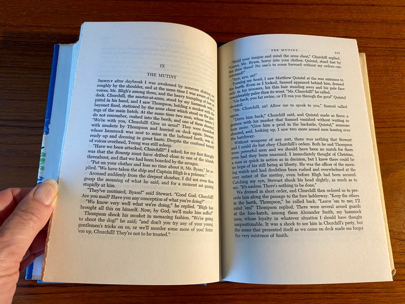 K&ouml;nnte beinhalten: Eine Nahaufnahme eines ge&ouml;ffneten Buches mit gelbem R&uuml;cken. Das Buch tr&auml;gt den Titel "The Mutiny" und der Text auf der Seite handelt von einer Meuterei auf einem Schiff. Der Text lautet "We've mutinied, Byanl!" said Stewart, "Good God, Churchill! Are you mad? Have you any conception of what you're doing?"
