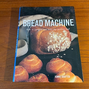 May include: A cookbook titled "Bread Machine: How to prepare and bake the perfect loaf" by Jennie Shapter. The cover features a close-up of a loaf of bread in a bread machine, along with several smaller rolls.