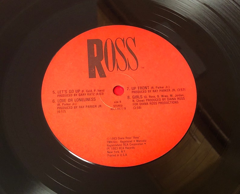 Pu&ograve; includere: Un'etichetta di disco in vinile rossa con la parola "ROSS" in grandi lettere bianche. L'etichetta elenca i titoli delle tracce e gli artisti del lato B del disco, tra cui "Let's Go Up", "Love or Loneliness", "Up Front" e "Girls".