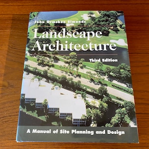 May include: A book titled "Landscape Architecture" by John Ormsbee Simonds, Third Edition. The cover features a photograph of a golf course and buildings. The subtitle reads "A Manual of Site Planning and Design."