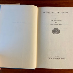 K&ouml;nnte beinhalten: Ein Buch mit dem Titel "Mutiny on the Bounty" von Charles Nordhoff und James Norman Hall. Der Buchumschlag ist wei&szlig; mit schwarzem Text und einer kleinen Illustration eines Schiffes.