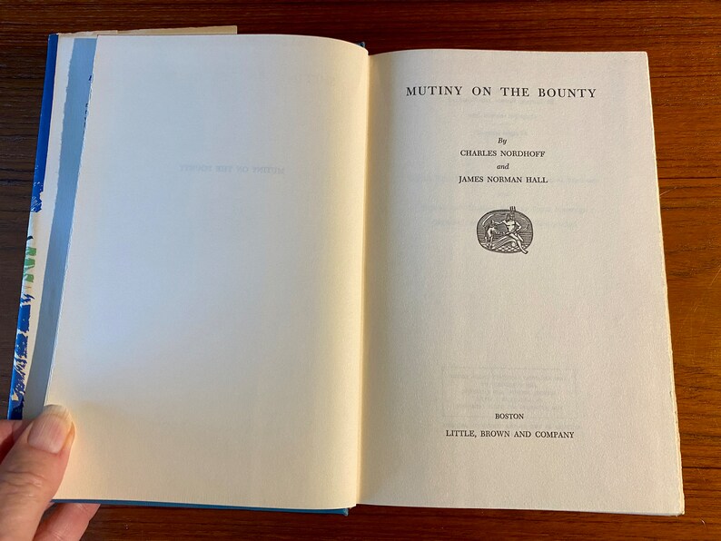 K&ouml;nnte beinhalten: Ein Buch mit dem Titel "Mutiny on the Bounty" von Charles Nordhoff und James Norman Hall. Der Buchumschlag ist wei&szlig; mit schwarzem Text und einer kleinen Illustration eines Schiffes.
